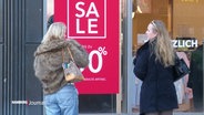 Zwei junge Frauen vor einem "Sale"-Schild eines Schaufensters. © Screenshot 