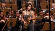 Eine Saxofonistin in einem Konzert. Im Hintergrund das Orchester. © Screenshot 