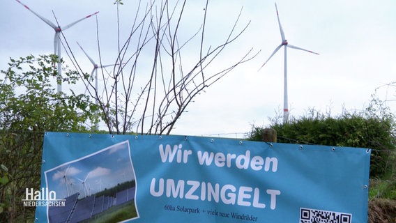 Ein Banner mit der Aufschrift: "Wir werden umzingelt" vor zwei Windrädern. © Screenshot 