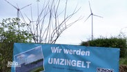 Ein Banner mit der Aufschrift: "Wir werden umzingelt" vor zwei Windrädern. © Screenshot 