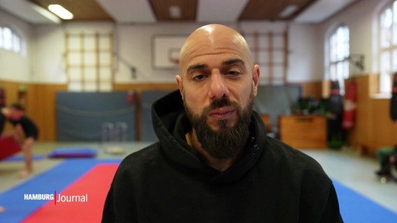 Trainer Syed Kareem Ahmed steht in einer Sporthalle. © Screenshot 