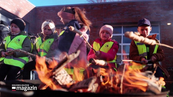 Kinder sitzen mit Warnwesten an einem Feuer und rösten Stockbrot über den Flammen. © Screenshot 