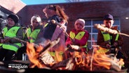 Kinder sitzen mit Warnwesten an einem Feuer und rösten Stockbrot über den Flammen. © Screenshot 