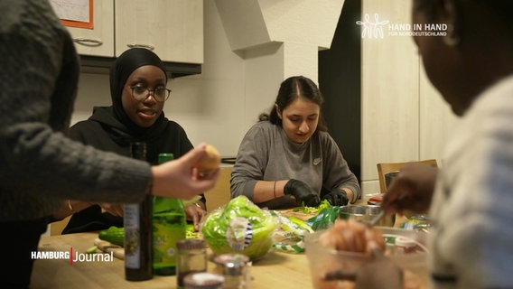 Mehrere junge Frauen sitzen an einem Küchentisch und kochen zusammen. © Screenshot 