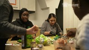 Mehrere junge Frauen sitzen an einem Küchentisch und kochen zusammen. © Screenshot 