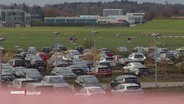 Mehrere Autos sind auf einem Stellplatz neben einem Flughafen-Rollfeld abgestellt. © Screenshot 