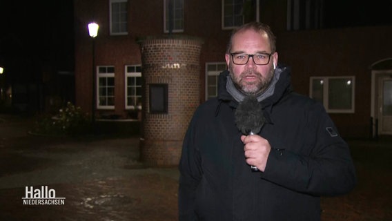 Reporter Sebastian Duden steht mit einem Mikro in der Hand im Dunkeln vor einem Haus. © Screenshot 