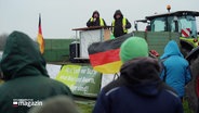 Bei einer Demonstration auf einem Acker hören viele Teilnehmende einer Rednerin auf einem Trecker-Anhänger zu. © Screenshot 