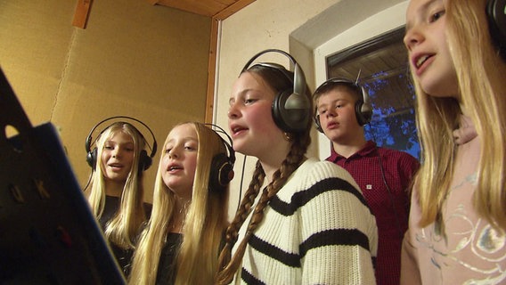 Vier Mädchen und ein Junge mit Kopfhörern auf den Ohren stehen in einem Tonstudio und singen. © Screenshot 