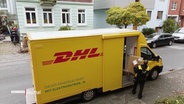 Ein DHL-Bote kommt mit einem Paket im Arm aus einem Lieferwagen. © Screenshot 