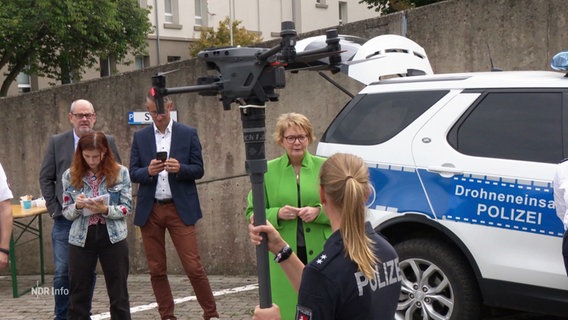 Eine Polizistin hält eine Drohne in der Hand, vor ihr stehen vier Personen. © Screenshot 