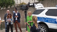 Eine Polizistin hält eine Drohne in der Hand, vor ihr stehen vier Personen. © Screenshot 