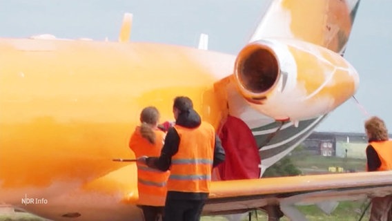 Ein mit orangener Farbe besprüter Privatjet. © Screenshot 