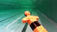 Eine orange Plastikpuppe sinkt in einem Schwimmbecken auf den Grund. © Screenshot 