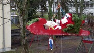 Ein Nikolaus in einem Holzschlitten, der durch Gurte gesichert mehrere Meter hoch in die Luft gezogen wird. © Screenshot 