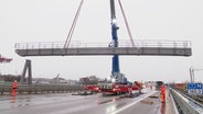 Ein Kran hebt eine neue Verkehrszeichenbrücke auf der gesperrten A7 in Hamburg an. © Screenshot 