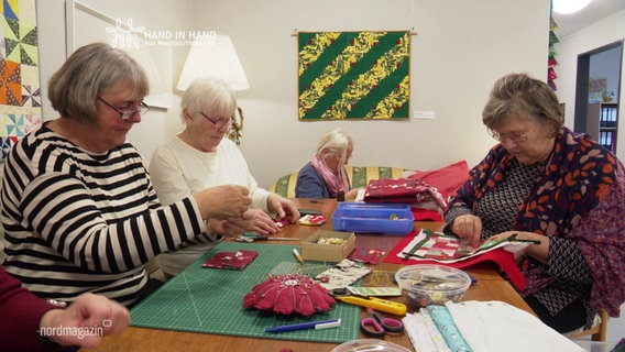 Vier Frauen sitzen an einem Tisch und nähen. © Screenshot 