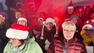 Ein Chor aus Weihnachtsmarktbesuchern singt Weihnachtslieder. © Screenshot 