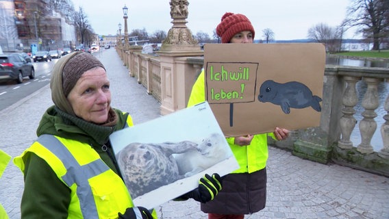 Zwei Mitglieder des BUND halten Plakate mit Robben in der Hand. © Screenshot 