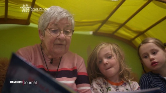 Eine Seniorin liest kleineren Kindern aus einem Buch vor. © Screenshot 