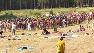 Auf einer größeren Waldlichtung haben sich im Sommer viele Menschen bei einem Wild-Camp in einem Pulk versammelt. © Screenshot 