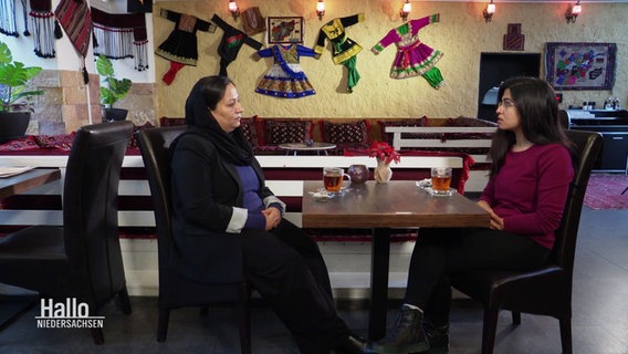 Zwei Frauen sitzen in einem Café gemeinsam an einem Tisch. © Screenshot 