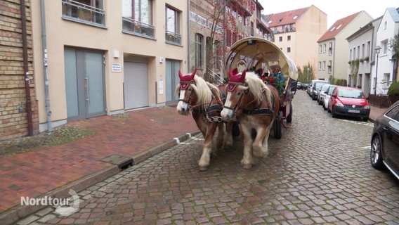 Zwei größere Pferde ziehen eine historische Pferdekutsche mit einem als Weihnachtmann verkleideten Kutscher durch eine Altstadtstraße. © Screenshot 