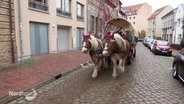 Zwei größere Pferde ziehen eine historische Pferdekutsche mit einem als Weihnachtmann verkleideten Kutscher durch eine Altstadtstraße. © Screenshot 