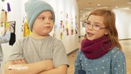 Zwei Kinder im Grundschulalter im Interview. Im Hintergrund sieht man einen Ausstellungsraum, in dem Bilder an den Wänden hängen. © Screenshot 