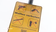 Ein gelbes Schild mit dem bildlichen und schriftlichen Hinweis, dass Waffen verboten sind. © Screenshot 