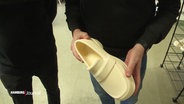 Eine Person hält einen 3D-gedruckten, weißen Schuh aus Thermoplast in die Kamera. © Screenshot 