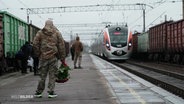 Ein Soldat in Uniform steht mit einem Strauß roter Rosen auf einem Bahnsteigu nd wartet auf einen einfahrenden Zug. © Screenshot 