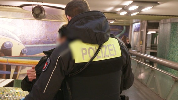 Ein Polizist durchsucht eine Person in einer U-Bahn-Station. © Screenshot 