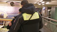 Ein Polizist durchsucht eine Person in einer U-Bahn-Station. © Screenshot 