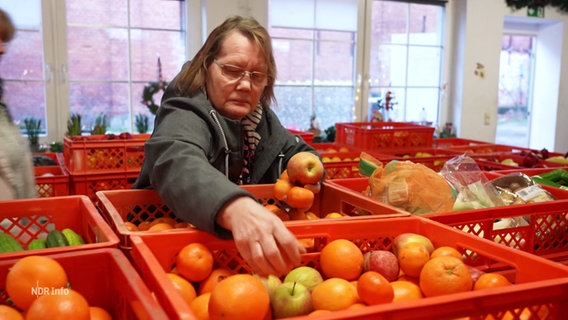 Eine Frau greift in eine rote Kiste voller Mandarinen. © Screenshot 