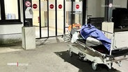 Eine obdachlose Person liegt notdürftig zugedeckt auf einem Krankenhausbett im Freien vor der Notaufnahme. (Quelle: Kältebus) © Screenshot 