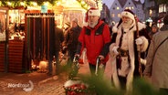 Zwei Weihnachtsmänner, einer am Rollator, laufen über einen Weihnachtsmarkt. © Screenshot 