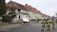 Einsatzkräfte der Feuerwehr stehen vor einem Reihenhaus, dessen Fassade durch eine Gasexplosion weggesprengt ist. © Screenshot 