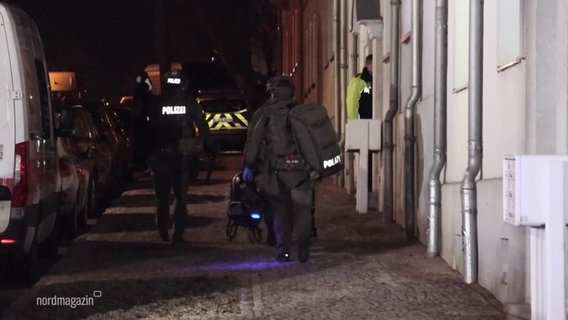 Mitglieder einer Polizeieinheit in Schutzuniform gehen einen Gehweg entlang. © Screenshot 