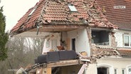 Ein durch eine Gasexplosion zerstörtes Haus. Im Obergeschoss steht noch eine Couch, aber die Außenwände fehlen komplett. (Aufnahme vom 20.12.2024 in Anklam). © Screenshot 