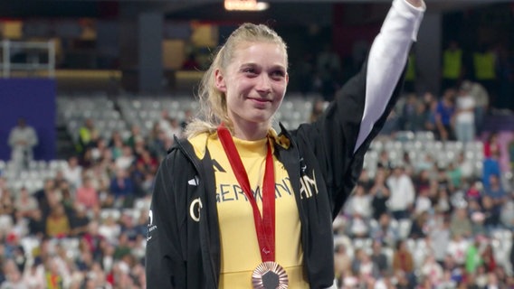 Die Sportlerin Lindy Ave trägt eine Bronzemedaille bei einer Siegerehrung im Stadion. © Screenshot 