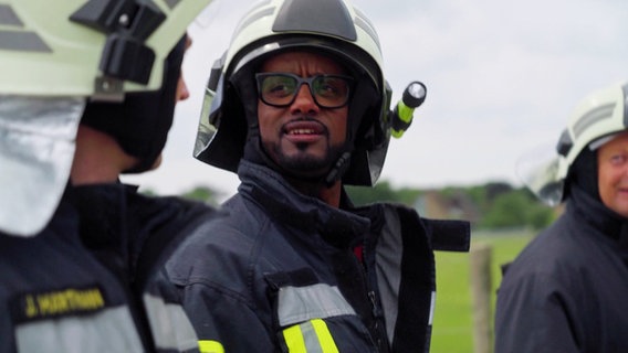 Yared Dibaba unterhält sich in Feuerwehr-Montur mit einem Feuerwehrmann. © Screenshot 