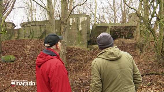 Zwei Männer schauen auf eine Ruine im Wald. © Screenshot 