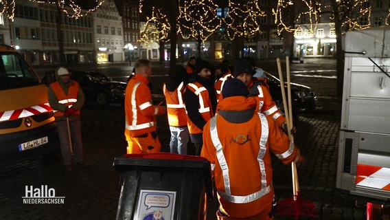 Mehrere Männer stehen mit Mülltonnen und Besen auf dem Rathausplatz. © Screenshot 