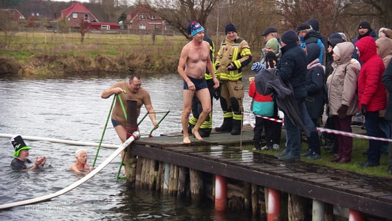 Teilnehmende beim Neujahrsbaden in Banzkow steigen aus dem kalten Wasser und werden von Schaulustigen empfangen. © Screenshot 