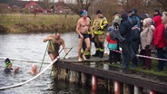 Teilnehmende beim Neujahrsbaden in Banzkow steigen aus dem kalten Wasser und werden von Schaulustigen empfangen. © Screenshot 