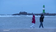 Zwei Menschen gehen bei stürmischem Wetter am Strand von Warnemünde. © Screenshot 