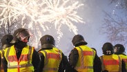 Mehrere Polizisten stehen beieinander, im Hintergrund explodiert Feuerwerk. © Screenshot 