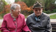 Das Ehepaar Christel und Gerhard Oppelt sitzt auf einer Bank vor seinem Haus. © Screenshot 