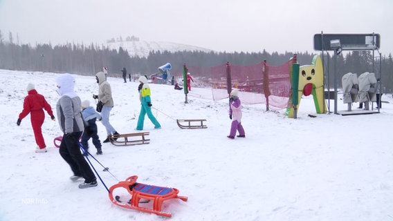 Viele Kinder ziehen ihre Schlitten den Berg hoch. © Screenshot 